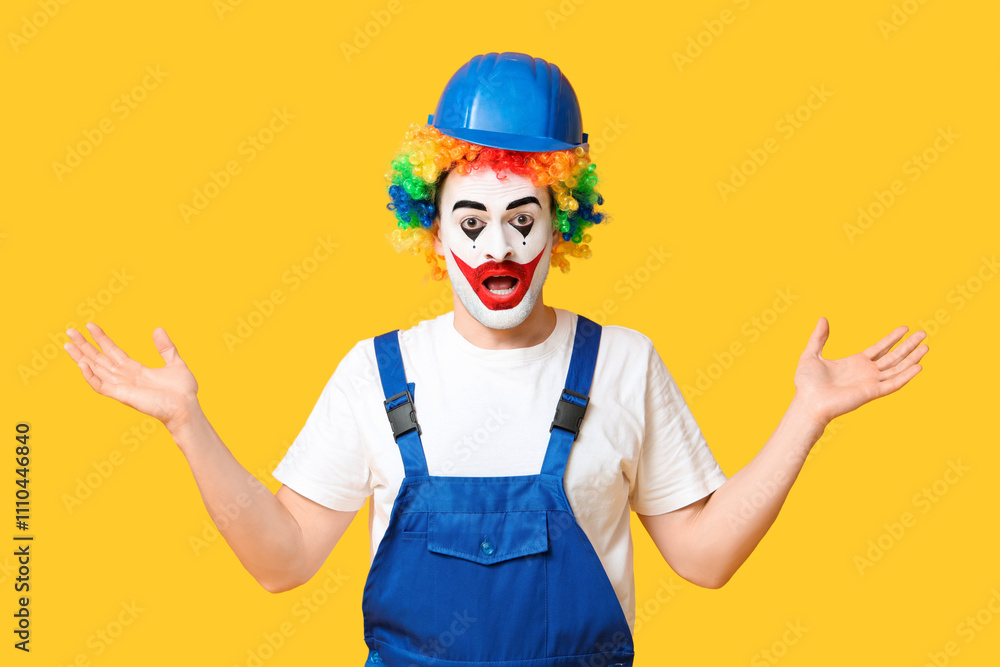 Fototapeta premium Surprised young man as clown in jumpsuit and helmet on yellow background