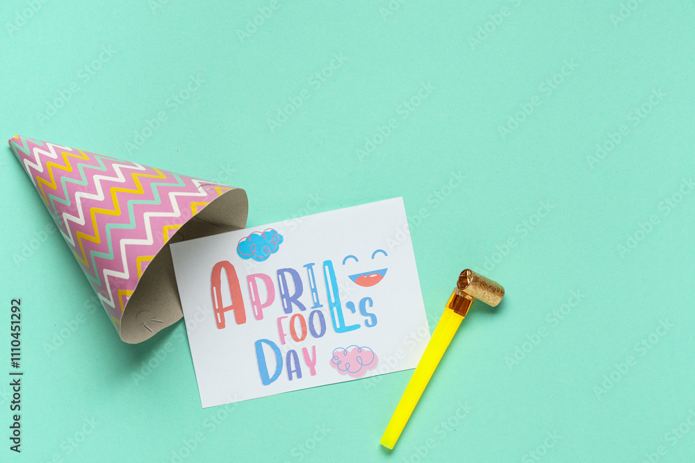 Fototapeta premium April Fool's Day greeting card with party hat and toy blower on pastel turquoise background, festive holiday flat lay with copy space