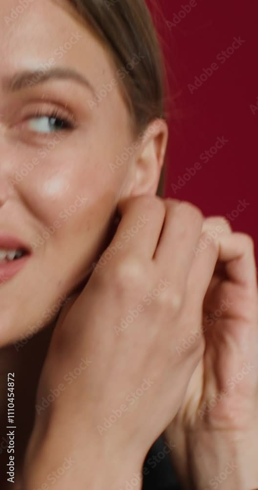 A woman in formal clothes puts on earrings while standing on a studio background. She smiles at the camera A woman in formal clothes puts on earrings while standing on a studio background. She smiles at the camera