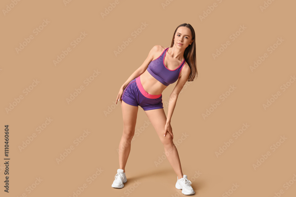 Young female trainer stretching on beige background Young female trainer stretching on beige background