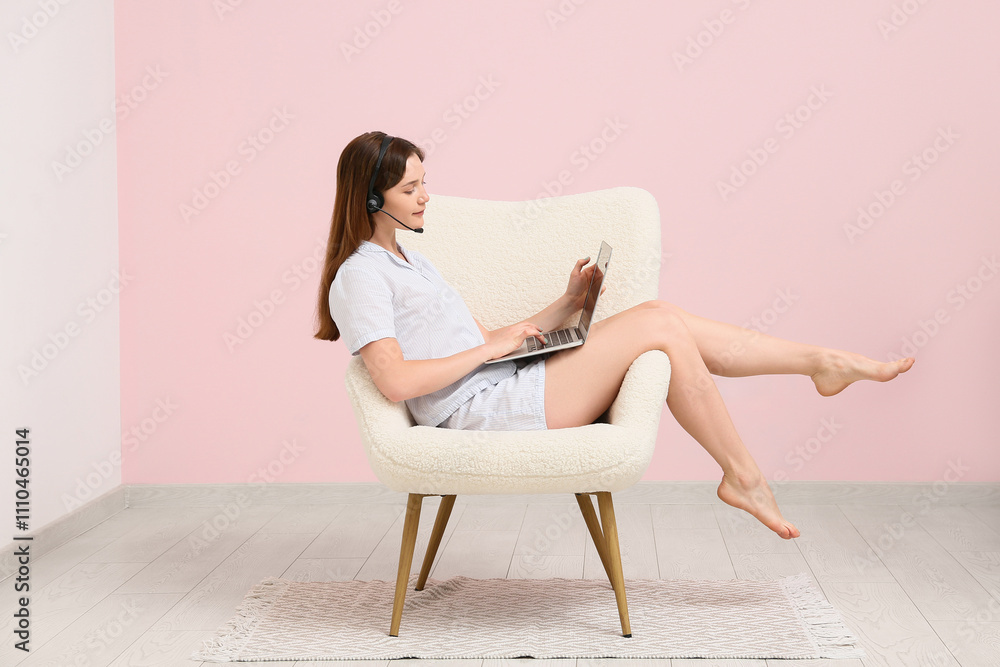 Young woman in pajamas and headset working with laptop and sitting on armchair at home. Remote work concept Young woman in pajamas and headset working with laptop and sitting on armchair at home. Remote work concept