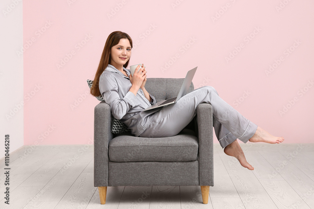 Young woman in pajamas working with laptop and holding cup of coffee on black armchair at home. Remote work concept Young woman in pajamas working with laptop and holding cup of coffee on black armchair at home. Remote work concept