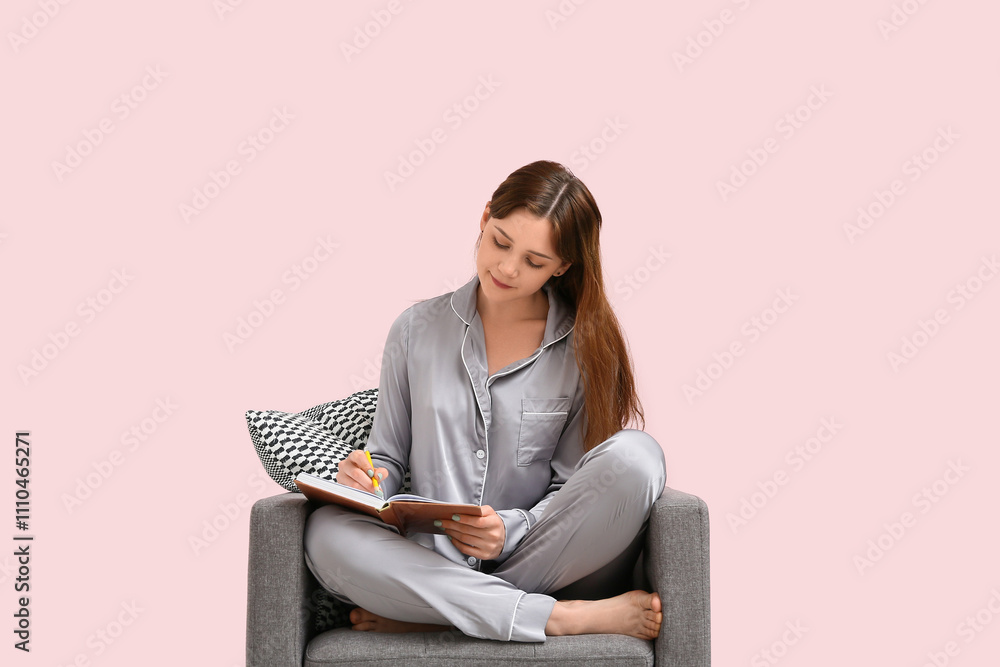 Young woman in pajamas writing in notebook on black armchair at home. Remote work concept Young woman in pajamas writing in notebook on black armchair at home. Remote work concept