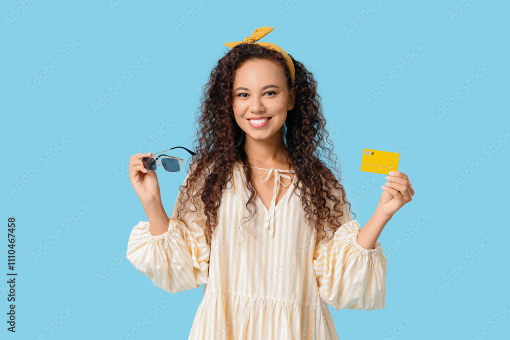 Beautiful African-American woman with sunglasses and credit card on blue background Beautiful African-American woman with sunglasses and credit card on blue background