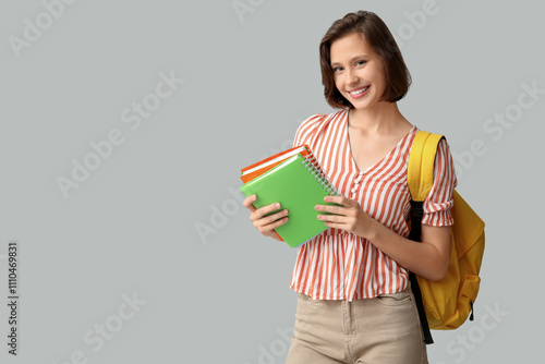 Beautiful female student with notebooks and backpack on grey background