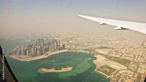 Airplane wing flying over desert area with capital city on coastline