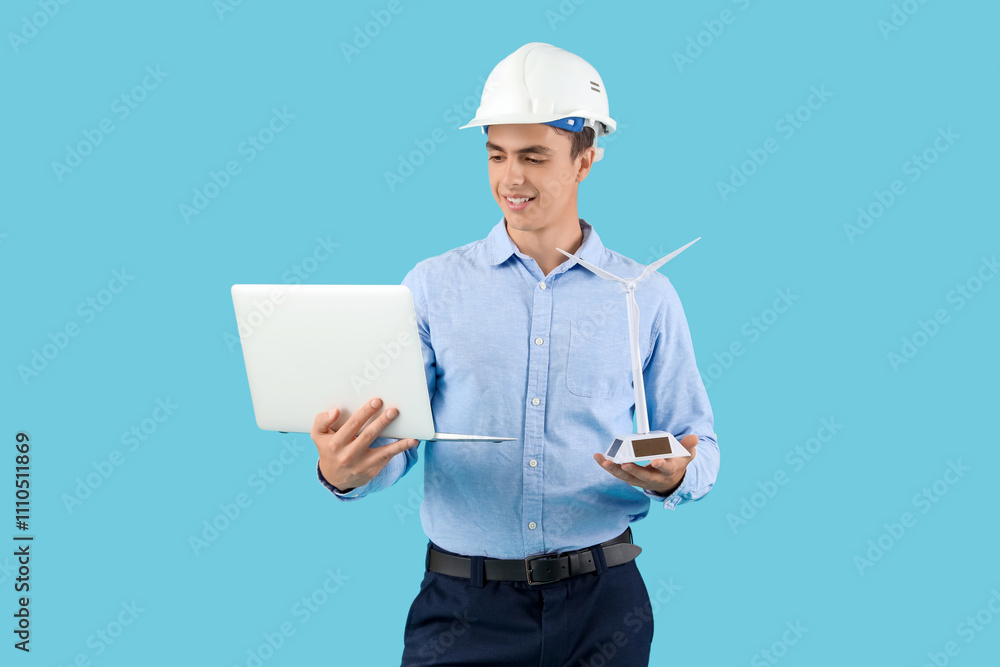 Male engineer with wind turbine model and laptop on blue background Male engineer with wind turbine model and laptop on blue background