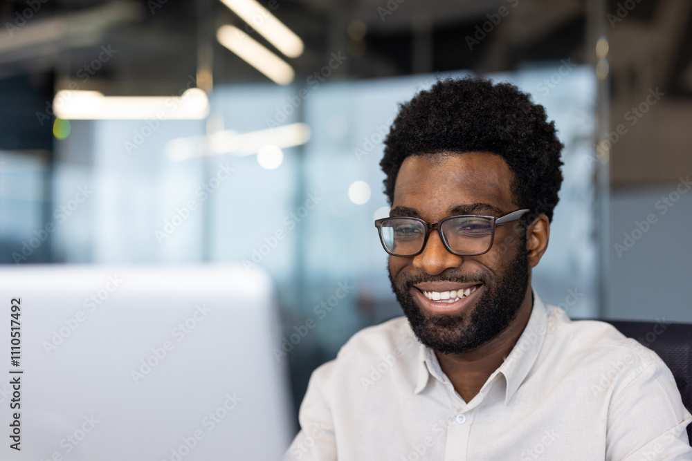 Obraz premium African American businessman smiling while working on computer in modern office. Glowing screen reflects focus, productivity. Professional attire highlights engagement, technology use.