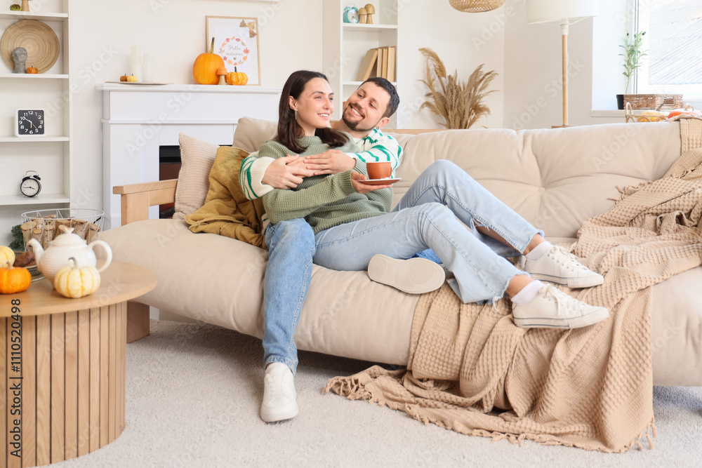Fototapeta premium Happy young couple with cup of tea sitting at home on autumn day