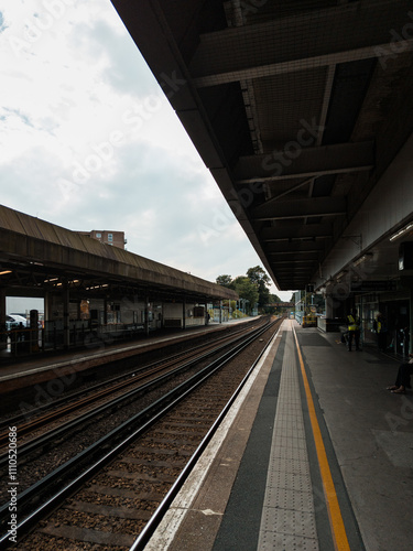 Empty Train Station Platform with Railway Tracks Stretching into the Distance on a Cloudy Day
