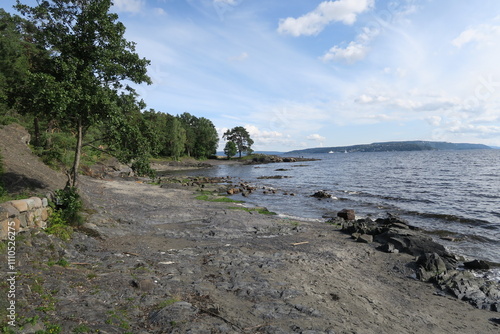 Auf der Insel Bygdoy im Stadtgebiet Oslos gibt es diese Bucht Paradisbukta. Dort reichen Bäume an den Oslofjord. Wellen branden an den Strand an einem warmen Sommertag. photo