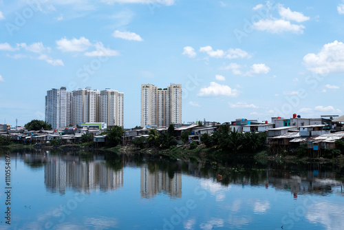 A mix of small, densely packed houses and tall modern buildings reflecting in a body of water under a clear blue sky, highlighting urban contrast and development.