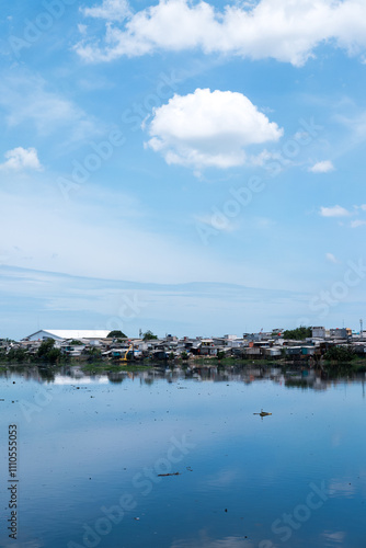 A mix of small, densely packed houses and tall modern buildings reflecting in a body of water under a clear blue sky, highlighting urban contrast and development.