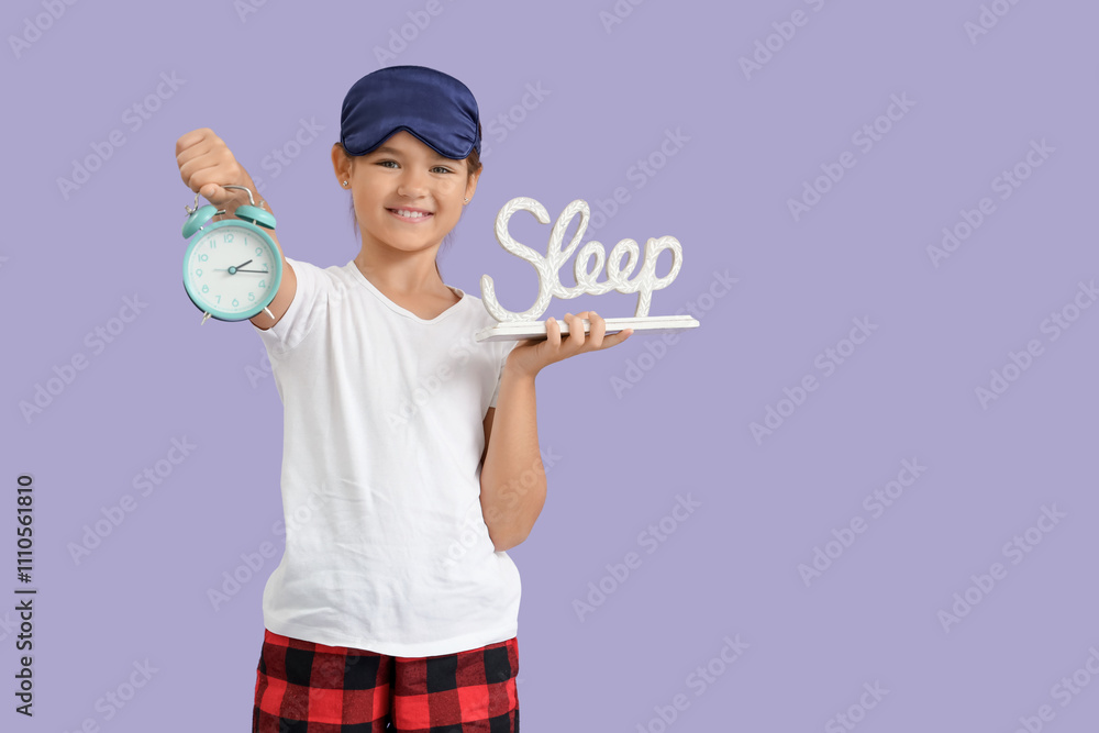 Cute little happy girl in pajamas with alarm clock and word SLEEP on purple background Cute little happy girl in pajamas with alarm clock and word SLEEP on purple background