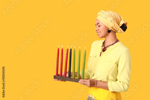 Young African-American woman with burning candles on yellow background. Kwanzaa celebration photo