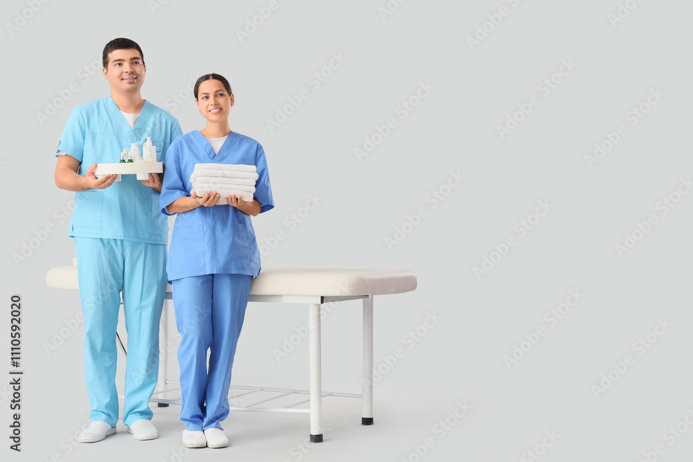 Massage therapists with spa supplies and couch on light background Massage therapists with spa supplies and couch on light background
