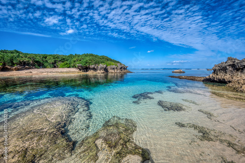 Crystal clear waters of Bise Beach, Motobu District, Okinawa main island. White sand beach with coral outcrops and small islands offshore.