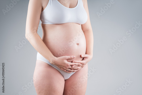 Pregnant woman with big belly in white underwear on gray background, pregnancy concept photo