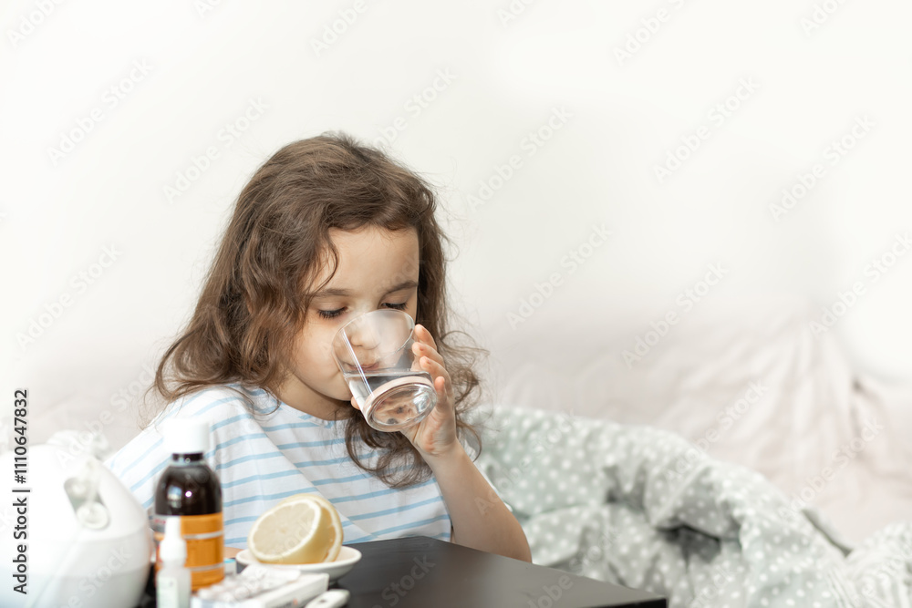 Sick sad little kid girl sits on bed at home and drinking water. Flu season. Healthcare concept. Sick sad little kid girl sits on bed at home and drinking water. Flu season. Healthcare concept.