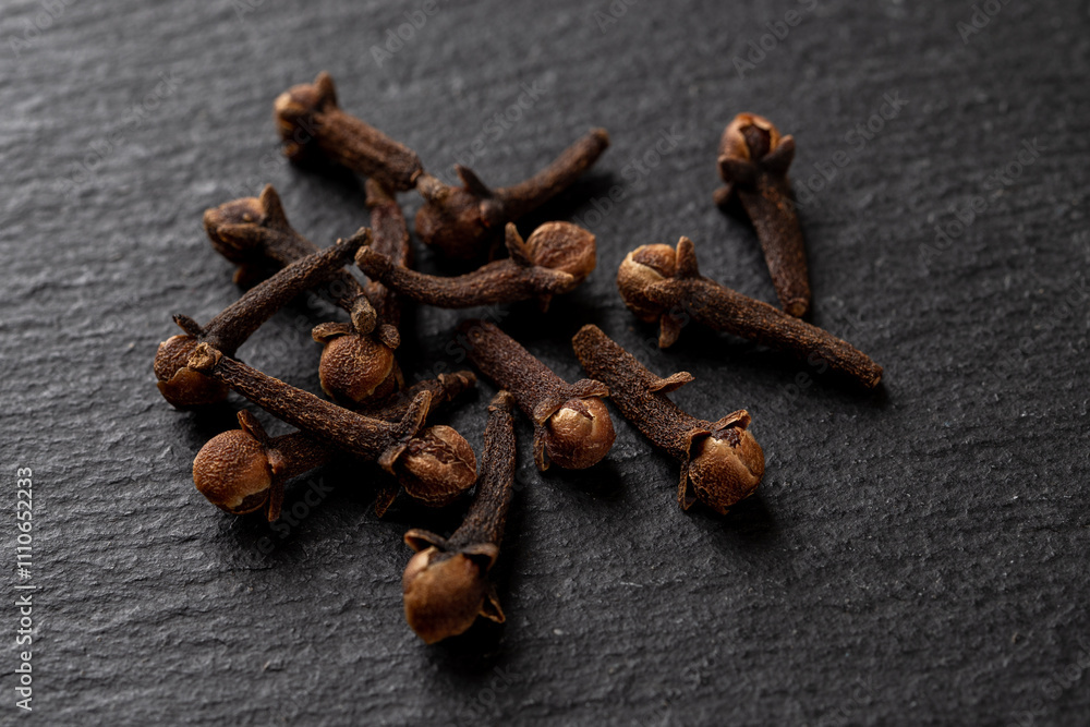 Fototapeta premium Whole cloves spice over black background. Heap of dry clove buds close-up. Syzygium aromaticum dry buds as ingredirnt for cooking. Macro. Spice concept.