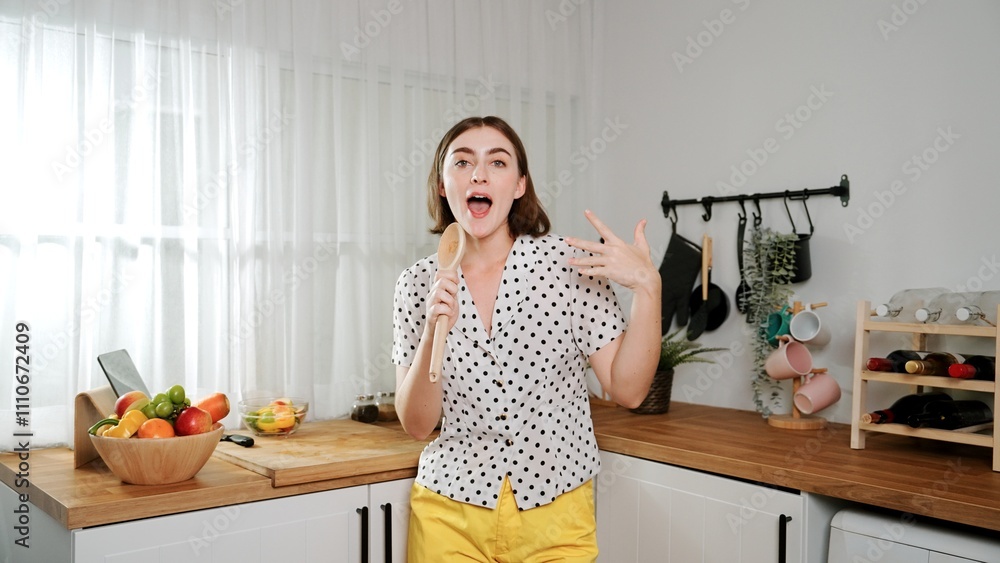 Energetic caucasian mother singing by holding ladle at modern kitchen while cooking and making salad for breakfast. Happy house keeper moving to music while prepare for making healthy food. Pedagogy. Energetic caucasian mother singing by holding ladle at modern kitchen while cooking and making salad for breakfast. Happy house keeper moving to music while prepare for making healthy food. Pedagogy.