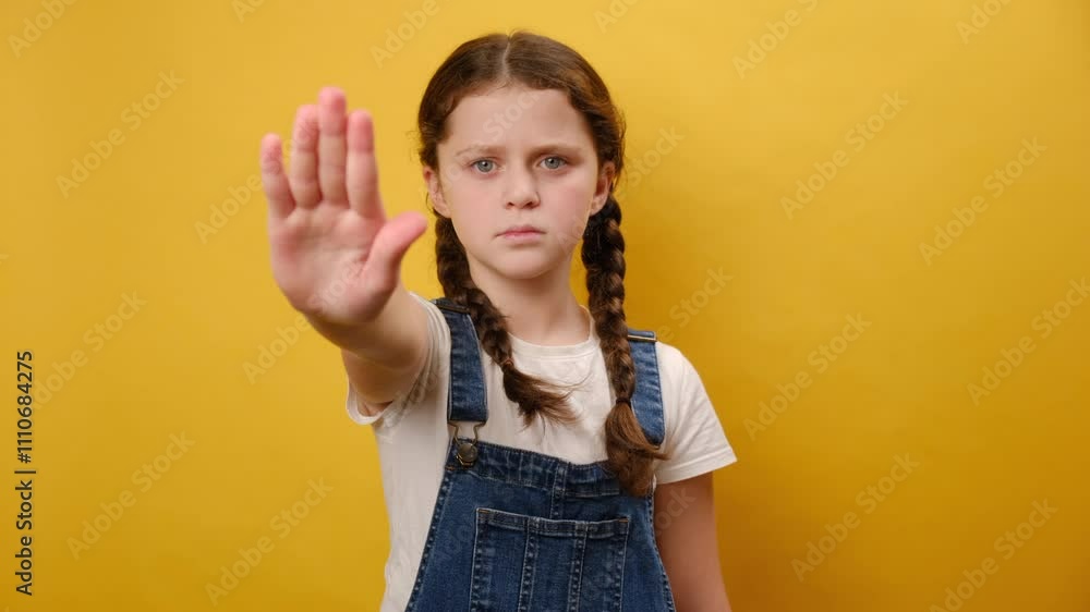 Portrait of serious strict preteen girl child showing to stop palm gesture refusing, posing isolated over plain yellow color background wall in studio. Childhood lifestyle concept Portrait of serious strict preteen girl child showing to stop palm gesture refusing, posing isolated over plain yellow color background wall in studio. Childhood lifestyle concept