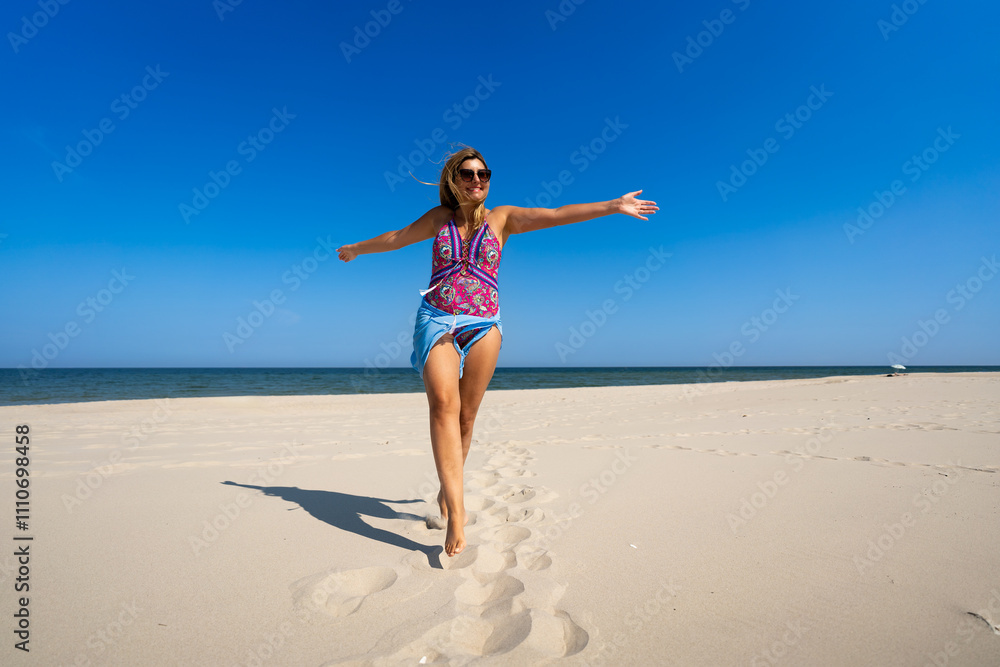 Beautiful middle-aged woman in swimsuit walking on sandy beach in summertime. Energy and happiness. Front view Beautiful middle-aged woman in swimsuit walking on sandy beach in summertime. Energy and happiness. Front view