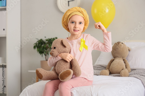 Little girl after chemotherapy with yellow ribbon and toy bear showing muscle...