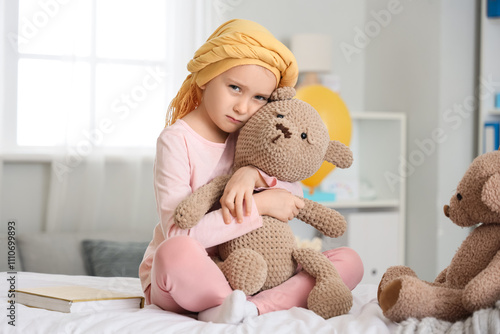 Sad little girl after chemotherapy with toy bear sitting in clinic. Childhood...