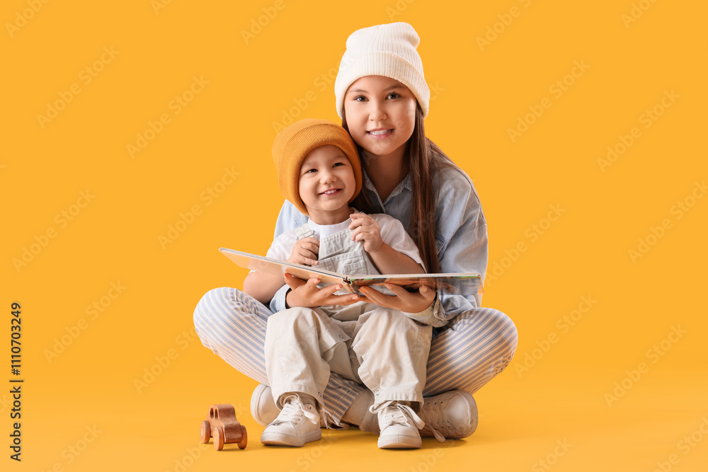 Teenage girl with her little brother reading story on yellow background Teenage girl with her little brother reading story on yellow background