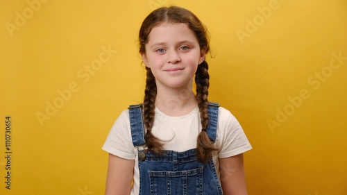 Portrait of happy pretty adorable preteen girl child, smiling looking at camera, posing isolated over plain yellow color background wall in studio. Childhood lifestyle concept