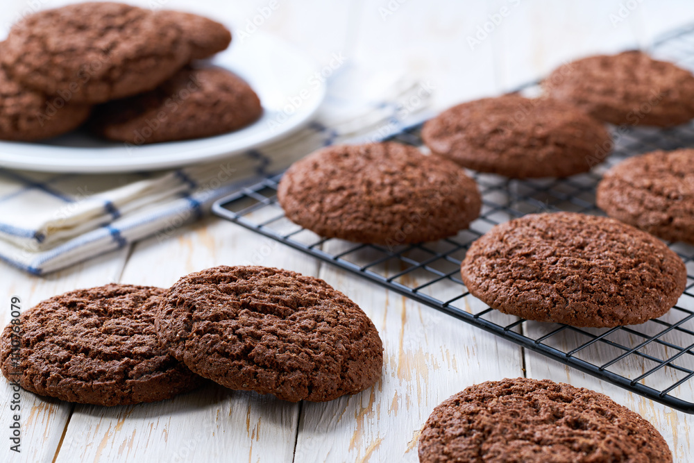 Fototapeta premium Traditional chocolate cookies are cooling after baking on a rack on a white table, selective focus.
