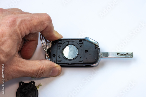 Bild auf Leinwand A man’s hand is holding a car key with the battery slot open, placed against a white background