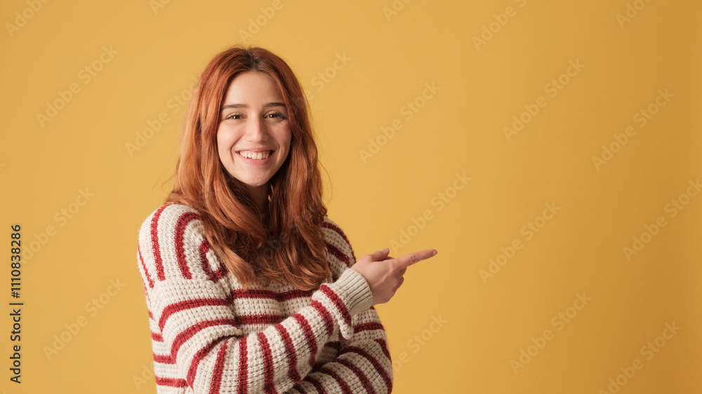Red-haired girl dressed in sweater, looking away to show mockup space on yellow background in studio. Beautiful girl poses in studio with blank space on yellow wall for your promotion Red-haired girl dressed in sweater, looking away to show mockup space on yellow background in studio. Beautiful girl poses in studio with blank space on yellow wall for your promotion