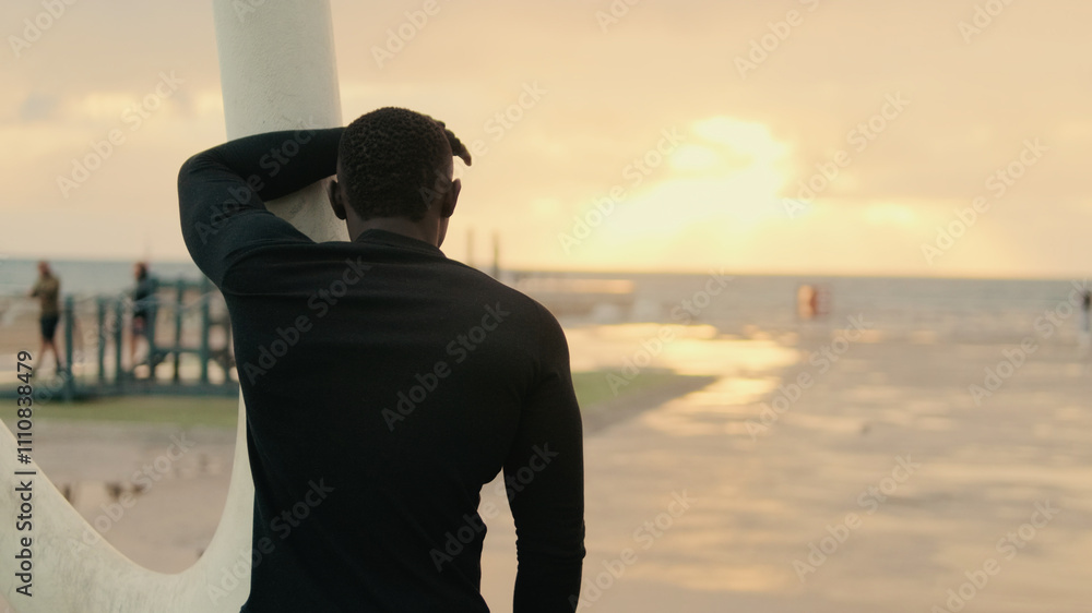 Fototapeta premium Back view of man resting between exercises during street workout by the sea, active lifestyle, sports motivation