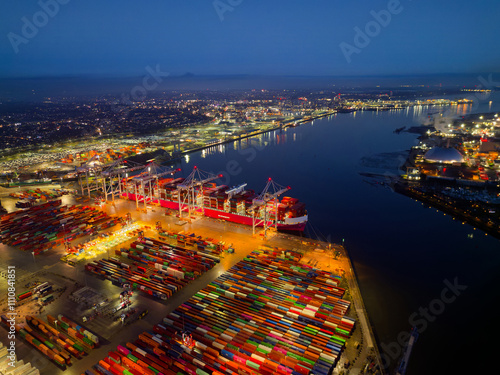 Obraz na płótnie Illuminated Southampton UK container terminal with large container ship at dusk. High altitude aerial view above bright commercial docks with lights towards waterfront city. Industrial backgrounds. w salonie