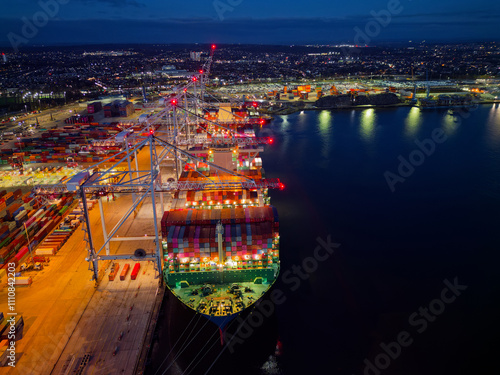 Obraz na płótnie Above bow of large container ship at Southampton Docks UK aerial view. Illuminated container terminal with cranes and lights reflection on calm sea. Beautiful cargo and shipping industrial background. w salonie