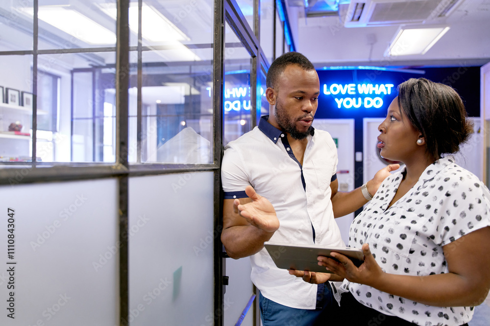 Attractive African American male model discussing with professional female agent in modern room near neon sign Attractive African American male model discussing with professional female agent in modern room near neon sign