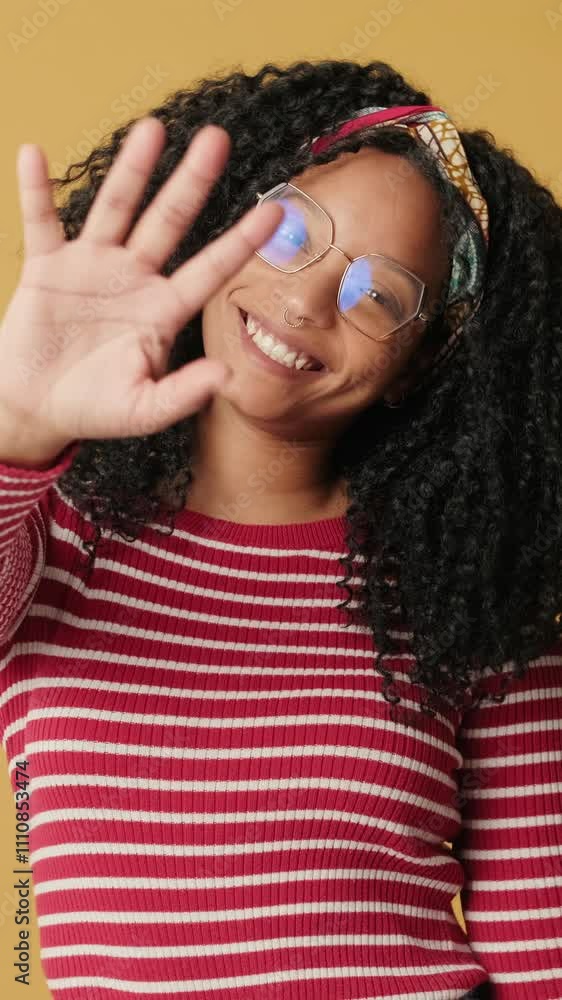 Young smiling woman waving her palm in greeting while standing on yellow background in the studio Young smiling woman waving her palm in greeting while standing on yellow background in the studio