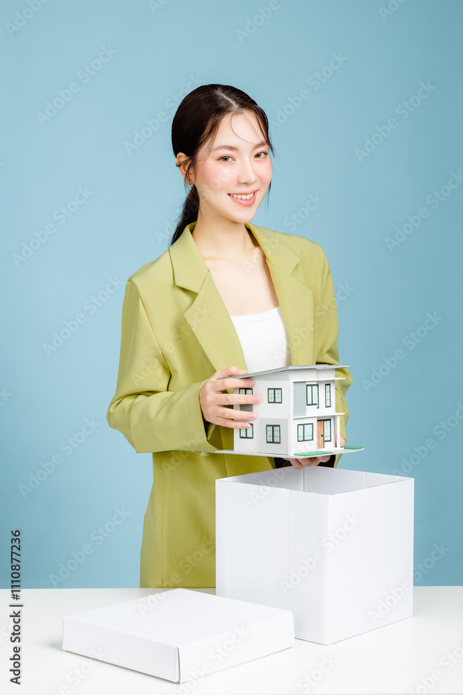 Young successful investor business woman in casual suit holding house model at white office desk with pc laptop isolated on pastel blue background studio portrait. Achievement concept Young successful investor business woman in casual suit holding house model at white office desk with pc laptop isolated on pastel blue background studio portrait. Achievement concept