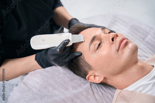 Handsome man visiting cosmetologist for ultrasonic scrubber treatment photo