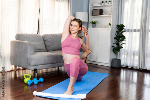 Flexible and dexterity woman in sportswear doing yoga position in meditation posture on exercising mat at home. Healthy gaiety home yoga lifestyle with peaceful mind and serenity.