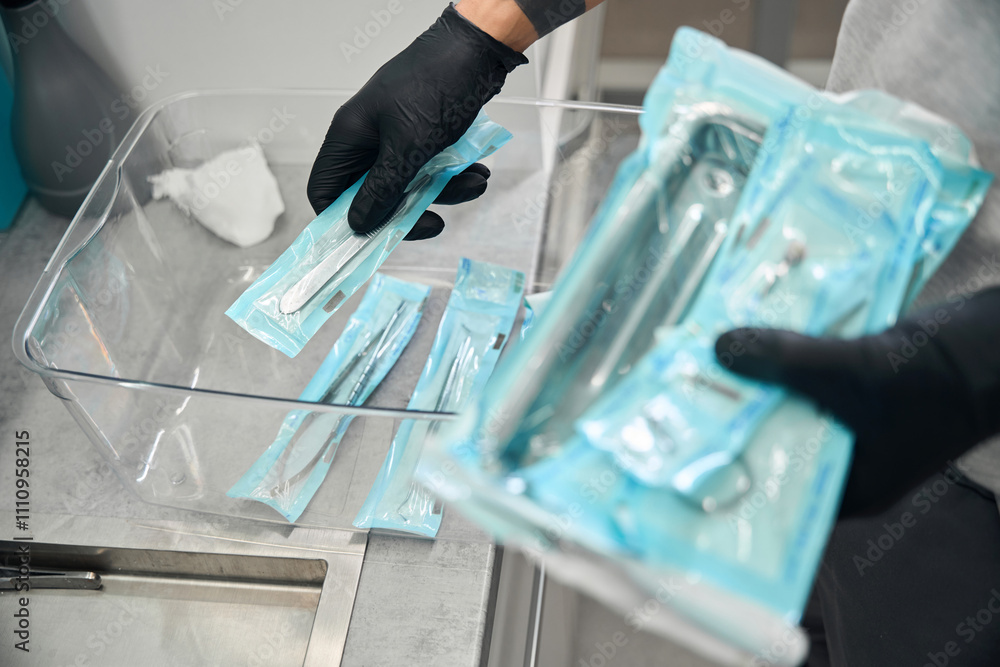 Dental technician in rubber gloves taking packages with sterile tools Dental technician in rubber gloves taking packages with sterile tools