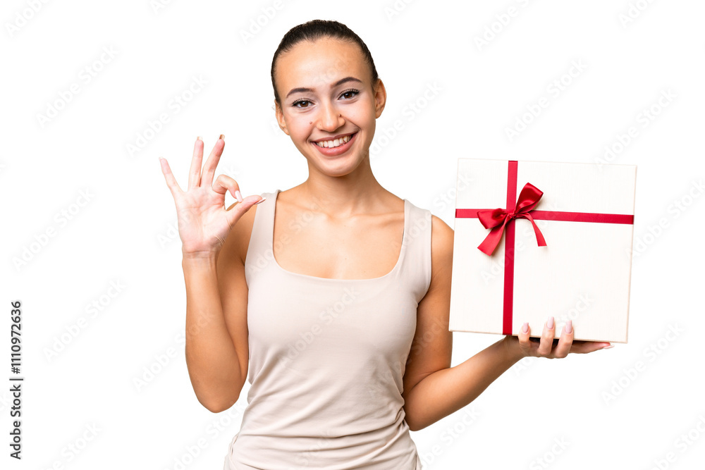 Young Arab woman holding a gift over isolated background showing ok sign with fingers Young Arab woman holding a gift over isolated background showing ok sign with fingers
