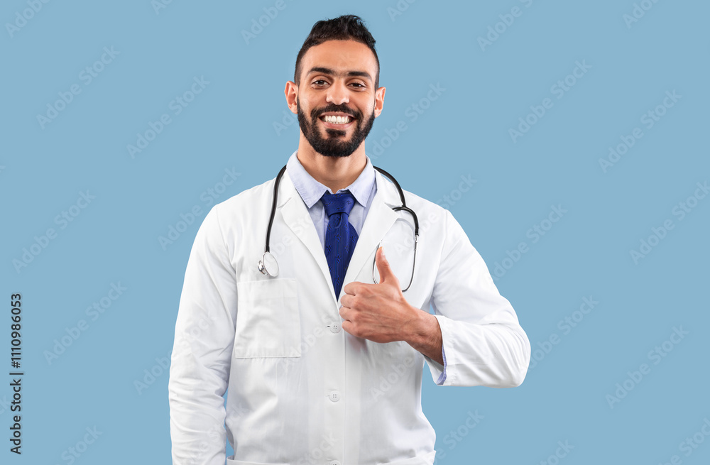 Happy Middle Eastern Doctor Man Gesturing Thumbs Up Smiling To Camera Posing Over Blue Studio Background. Portrait Of Professional Physician. I Like Medical Career Concept Happy Middle Eastern Doctor Man Gesturing Thumbs Up Smiling To Camera Posing Over Blue Studio Background. Portrait Of Professional Physician. I Like Medical Career Concept