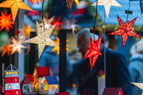 Besucher auf einem Weihnachtsmarkt vor einem Satand mit leuchtenden Sternen zum Verkauf photo