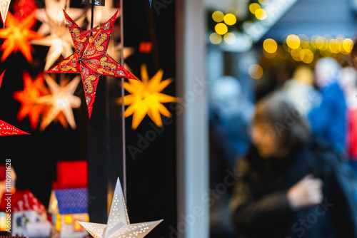 Besucher auf einem Weihnachtsmarkt vor einem Satand mit leuchtenden Sternen zum Verkauf photo