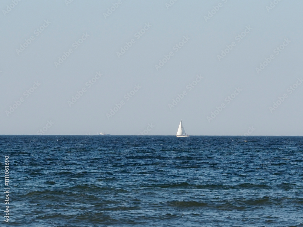 Serene sailboat on the horizon of a calm blue sea under a clear sky on a sunny day Serene sailboat on the horizon of a calm blue sea under a clear sky on a sunny day