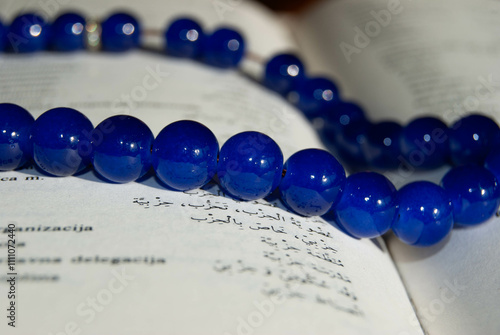 A detailed view of blue prayer beads against softly blurred Arabic text, creating a serene and spiritual ambiance. photo