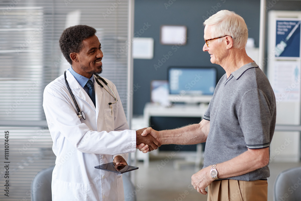 Obraz premium Waist up portrait of smiling African American doctor greeting elderly male patient and shaking hands during consultation at clinic, copy space